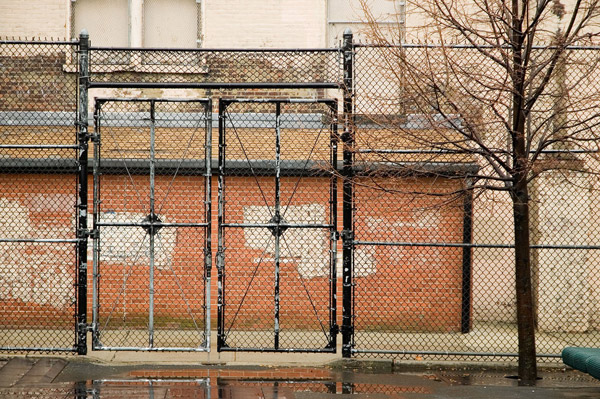 Schoolyard fence gates stand in front of a brick
wall.