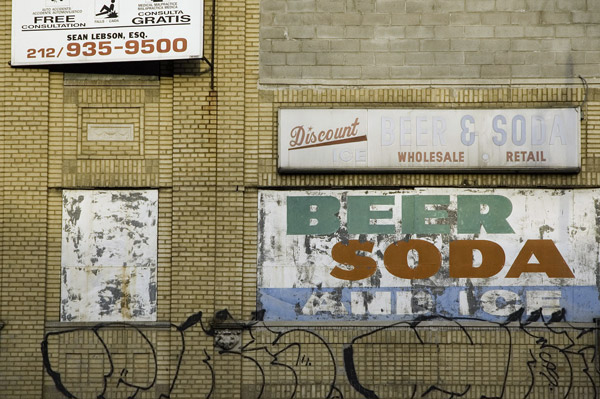 Signs on a yellow brick wall advertise beer, soda, and
ice.