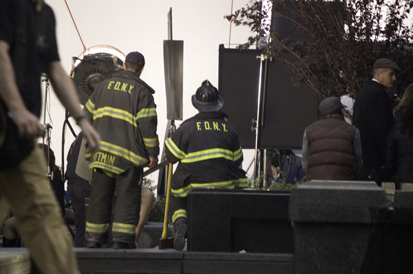 Extras in fire department gear wait behind lighting
equipment.