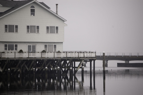 A house sits on stilts over water, with a bridge in the
background.