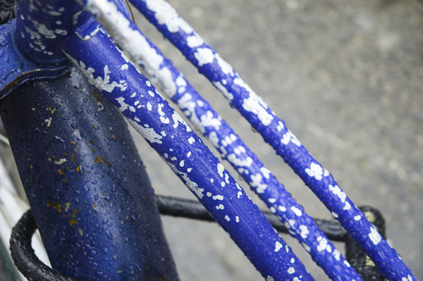 A blue bike with white speckles glistens with raindrops.