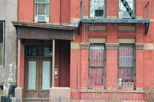 The roof over the entrance of a brick house tilts.