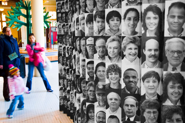 Museum visitors stand next to a display of photos of people
of various ethnic backgrounds.