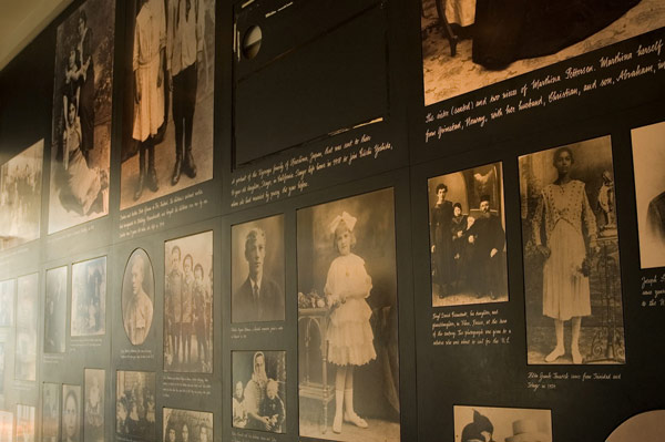 A wall of photos of immigrants' portrait photographs.