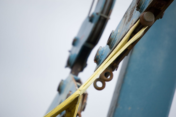 The yellow strap of a boat launch hangs from blue
metal.