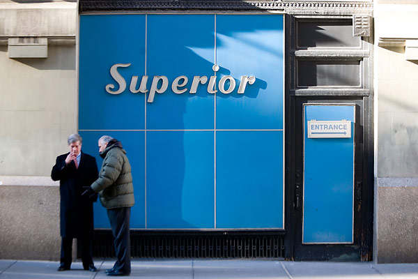 Two men talk, one of them smoking, outside a blue
storefront.