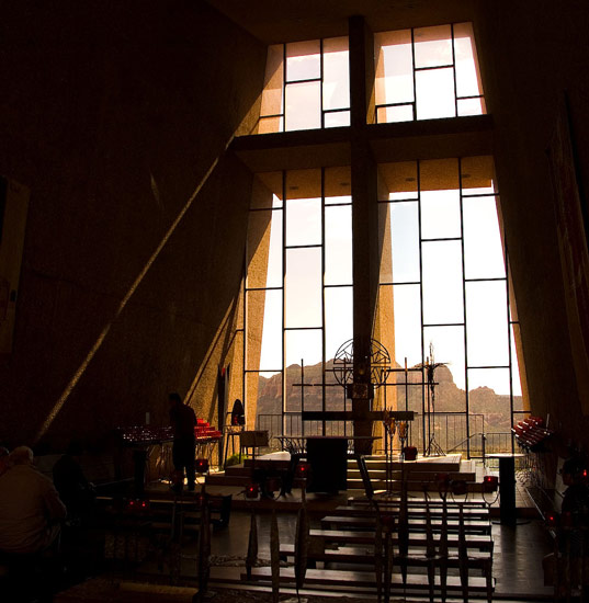 A large cross is in silhouette against the glass panes of a
chapel window.