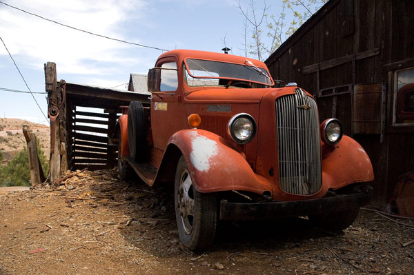 An old red pick-up truck sits in a brown dirt yard.