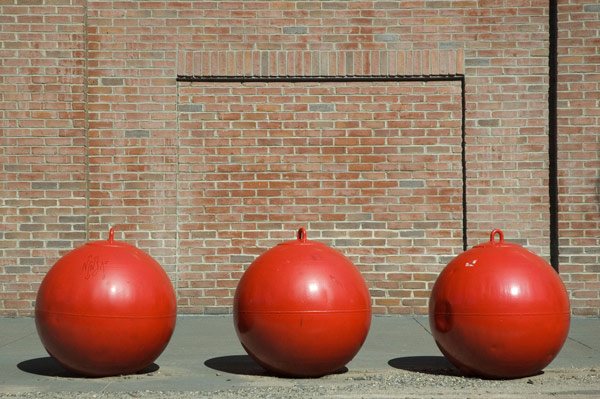 A trio of red buoys against a brick wall.