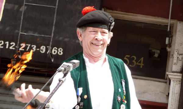 A man in a tam o'shanter twirls a flaming baton.