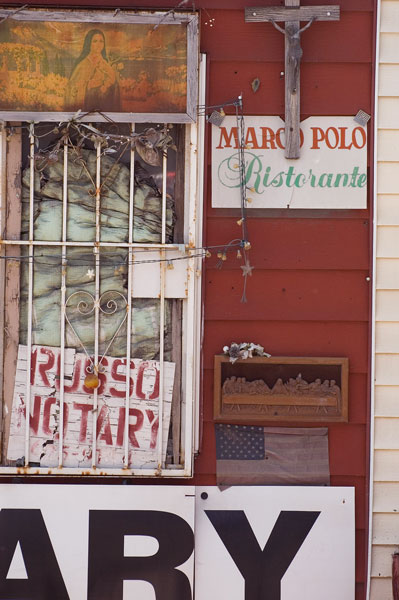 A crucifix, Last Supper scene, American flag, and weathered
signs on a red wall.