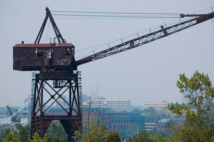 An abandoned loading crane has a city skyline behind it.