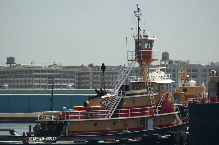 A brightly colored tugboat with warehouses in the
background.