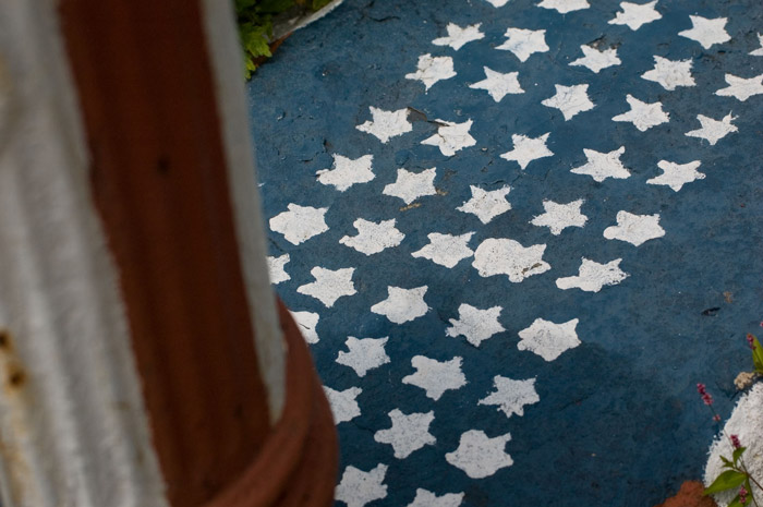 A sidewalk has badly-painted white stars on a blue field,
next to a red and white fire hydrant.