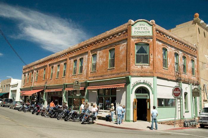 A corner hotel has bystanders and motorcycles outside.