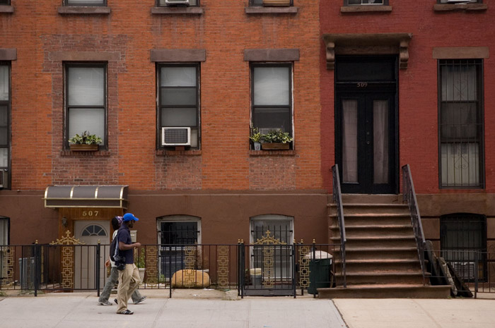 Pedestrian in a Mets cap walking past brick row houses.