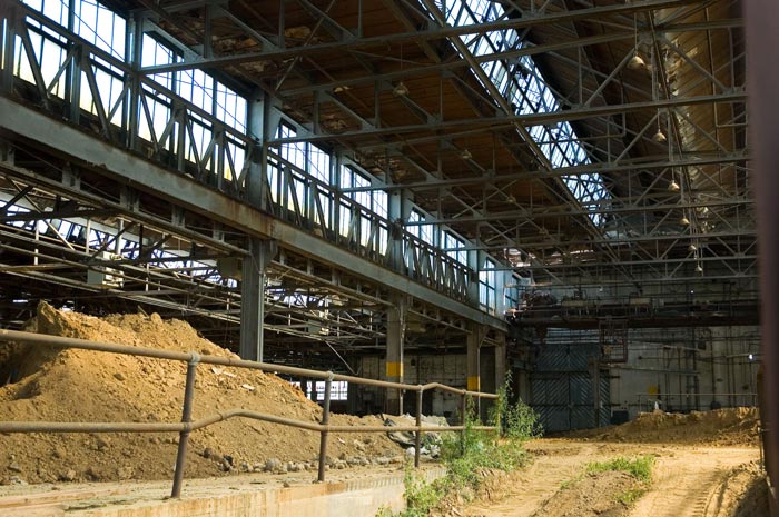 Light shines down on the dirt floor of an empty factory.