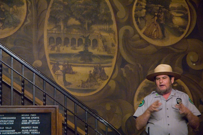 A guide gestures while talking in front of a mural.