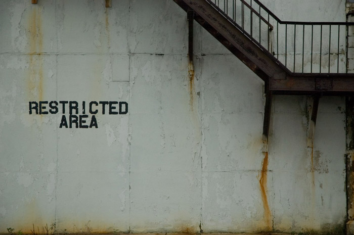 A wall is blank, save for a sign reading, 'Restricted Area.'