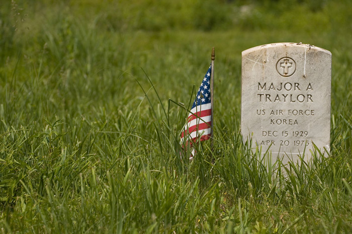 A veteran's tombstone, with a small American flag by its side.