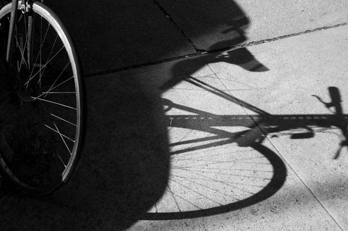 A bike, locked against a metal sign pole, with its shadow.