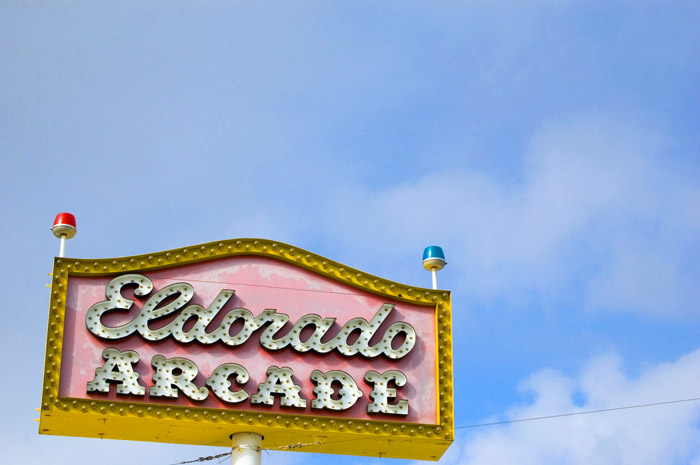 A faded pink sign with lights, against a powder blue sky.