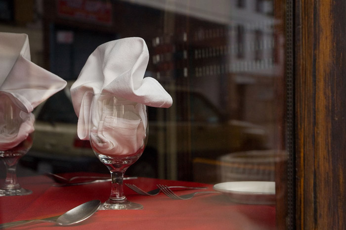 A white napkin, stuffed in a wine glass, on a red table cloth.