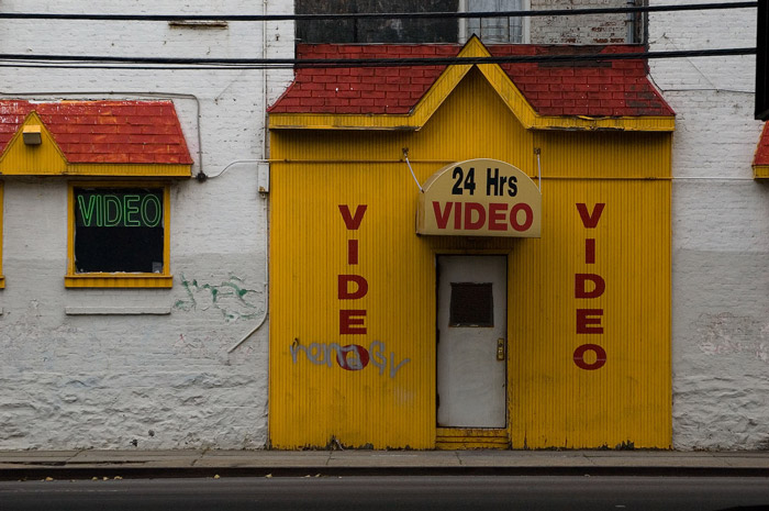 A storefront with almost no windows offering videos, 24 hours.