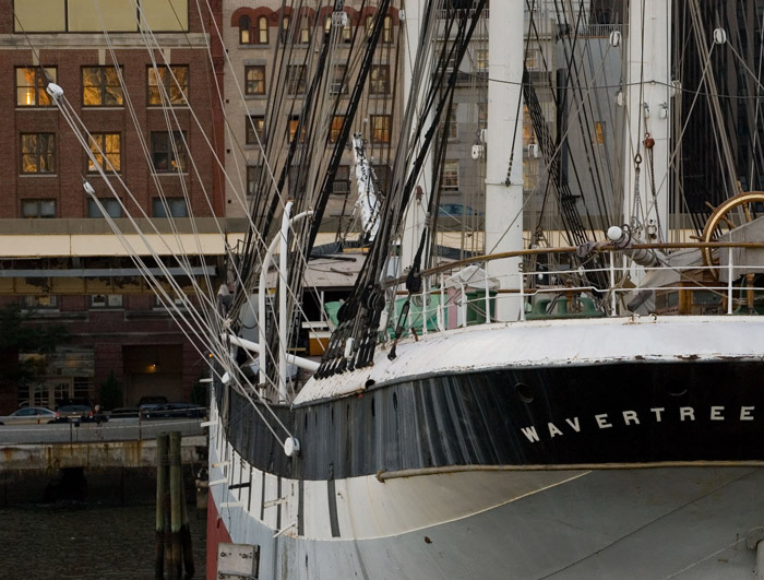 A ship's bow, masts, and cables, with Manhattan in the back.