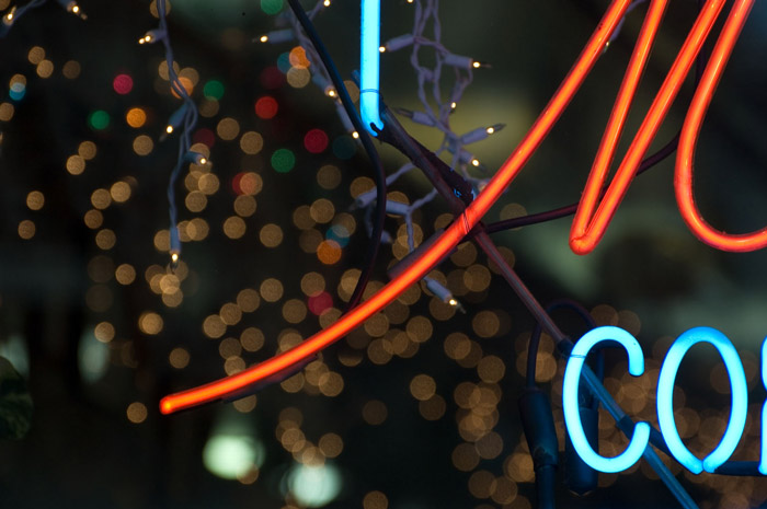 The swoop of a red 'M' in a neon sign, with Christmas lights in back.