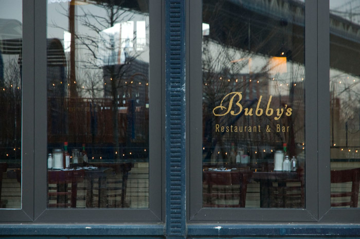 The Manhattan Bridge is reflected in two restaurant windows.