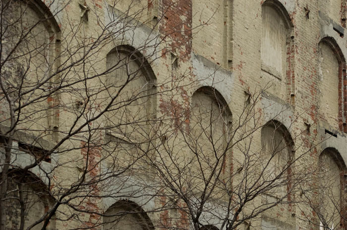 An old warehouse's arched windows are bricked up, and much of the brick is exposed.