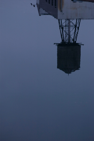 The water of the Gowanus Canal shows the upside down reflection of a water tank.