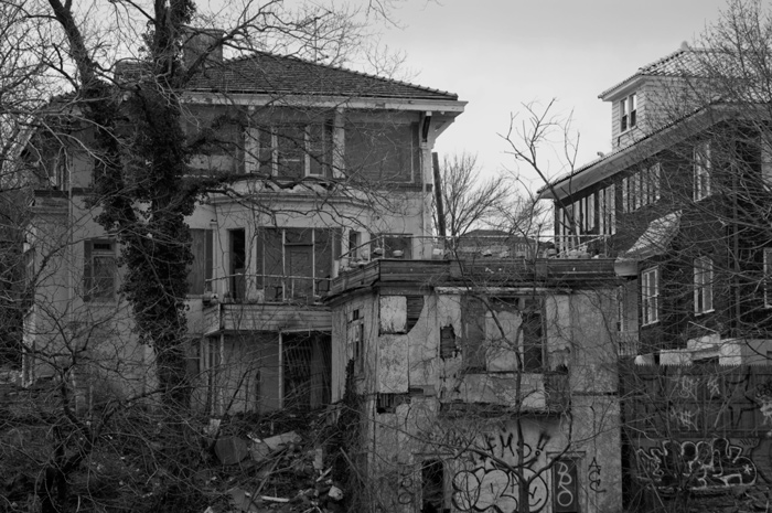 An abandoned multi-level home has a decayed facade and has been painted with graffiti.