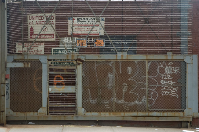 A tall fence gate is closed, but covered with graffiti.