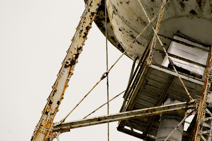 An intricate network of rusting supports holds up a water tank underbelly.