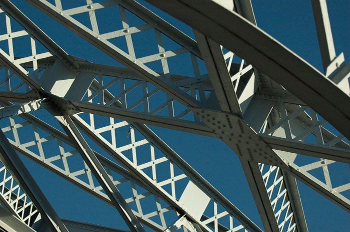 Crossing 'x' patterns within girders, all supporting a bridge, against a blue sky.