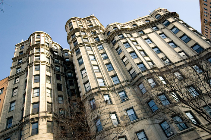 A tall apartment building with a wavy front of bay windows faces into the sun.