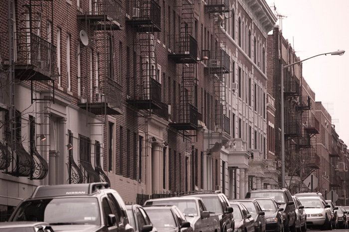 Row houses and parked cars line a street on a gently sloping hill.