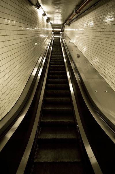 Looking up through glossy tiled walls, an escalator rises to the back.