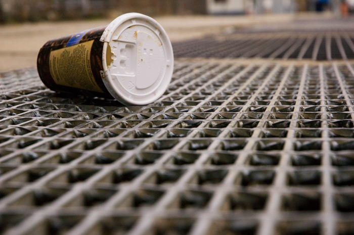 A paper coffee cup lays on its side, on a sidewalk grate.