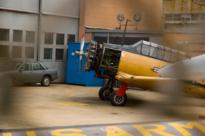 In a yard behind a fence, an old World War Two fighter plane's engine is opened up for educaitonal purposes.