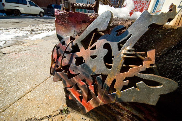 A metal sculpture has been attached to concrete and spray-painted a variety of colors.