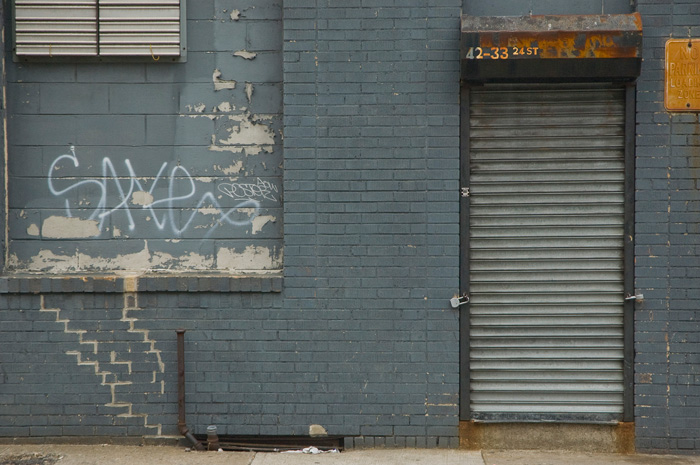 A door's roll-down front has been lowered and padlocked. Rust abounds, and what isn't rusty is grey and covered with graffiti.