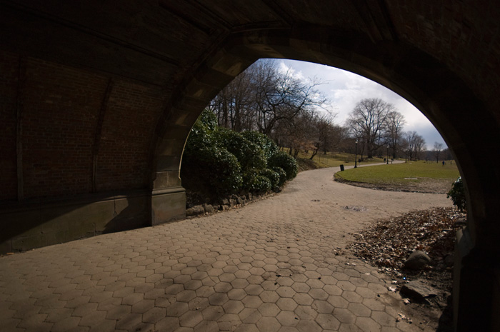 A short tunnel, mostly in the dark, has an arched exit onto a broad park meadow.