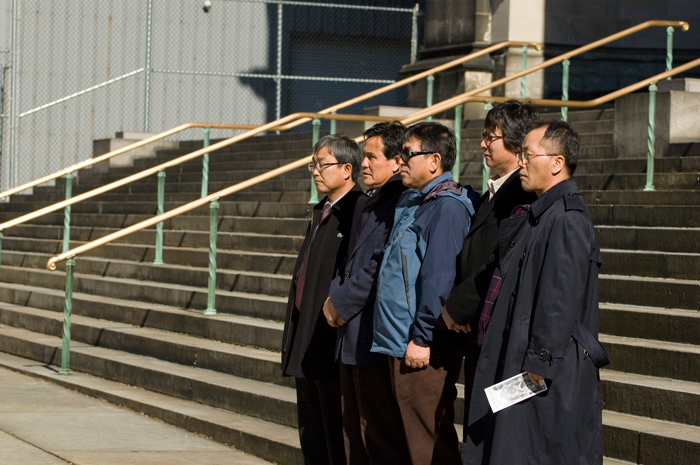 Five unsmiling tourists in a row pose for a photograph in front of a major tourist attraction.