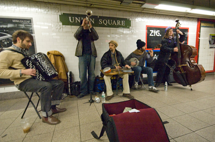 A jug band of five musicians entertains passers-by on the mezzanine of a New York City subway station.