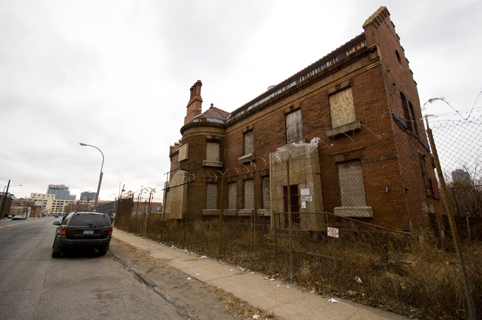 A small brick building on an isolated street has interesting architecture, but its windows have been boarded up, and it's been fenced off.