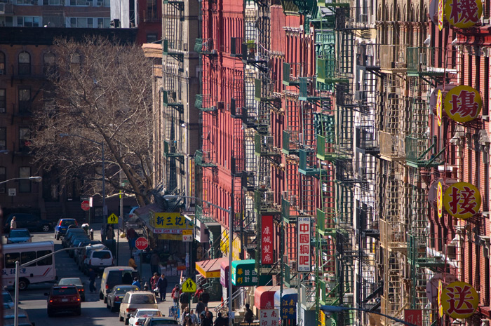 A Chinatown street's tenements are painted in bright, different colors, with complementary colors on their fire escapes.