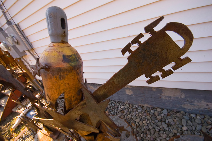 An iron sculpture of an electric guitarist, where the person's body is made from a tall gas tank.